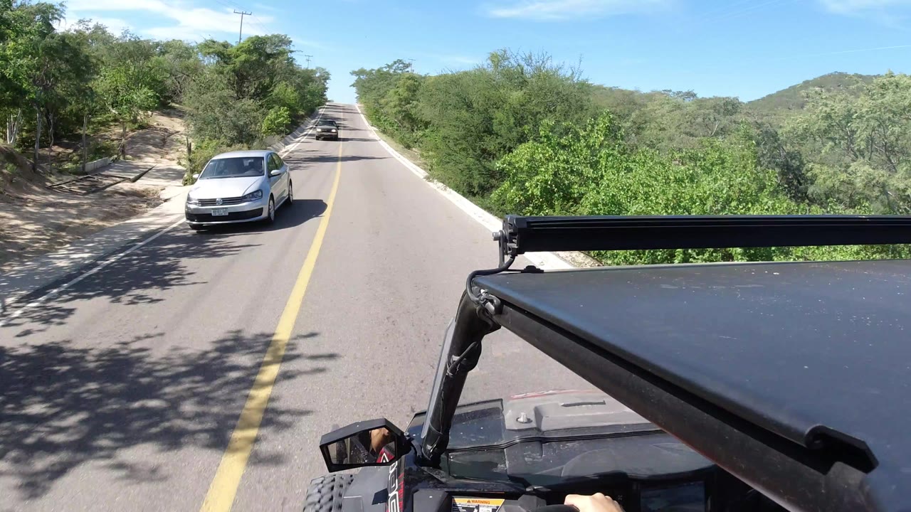 Wrangler roof foreground on a sunny two-lane road with a white car approaching.
