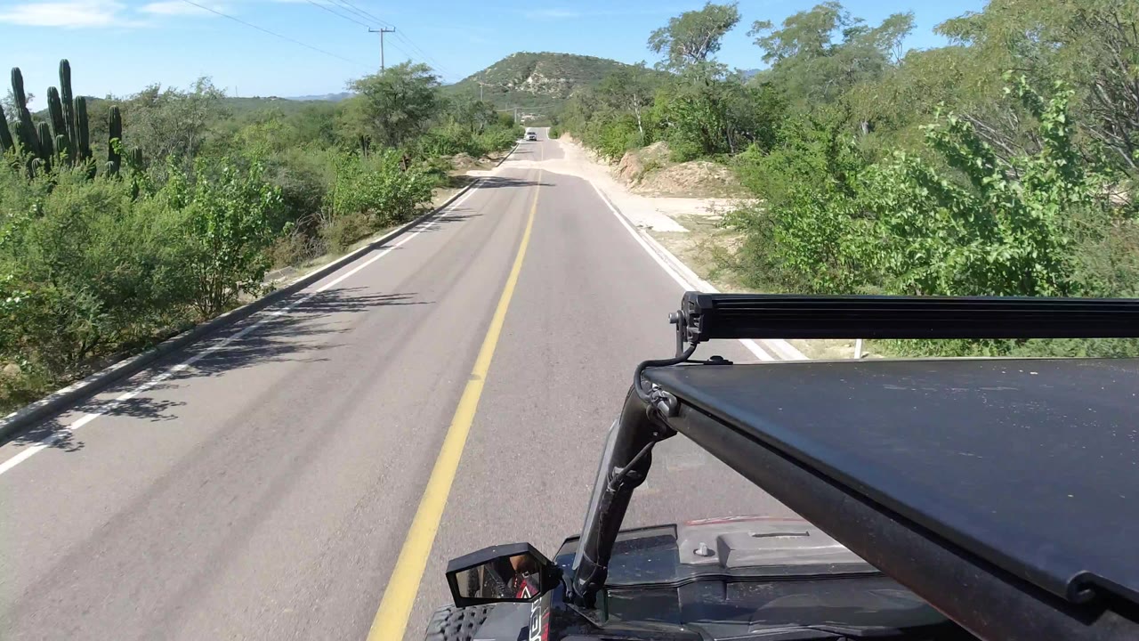 Forward view down a paved rural road from an open vehicle.