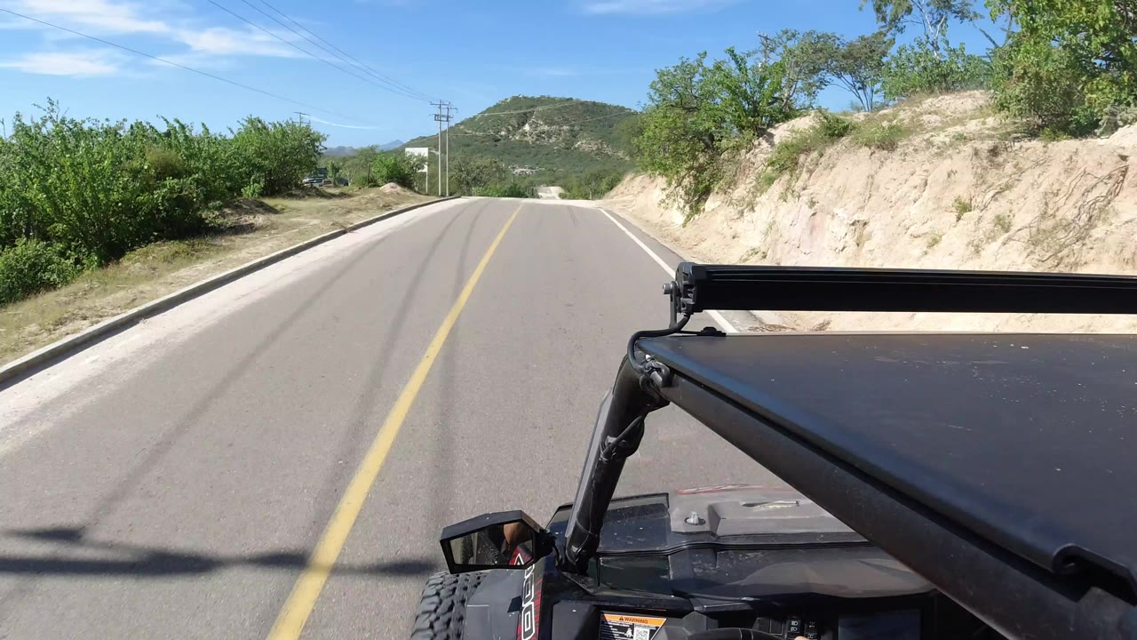 Jeep-mounted view down a paved country road toward low green hills.
