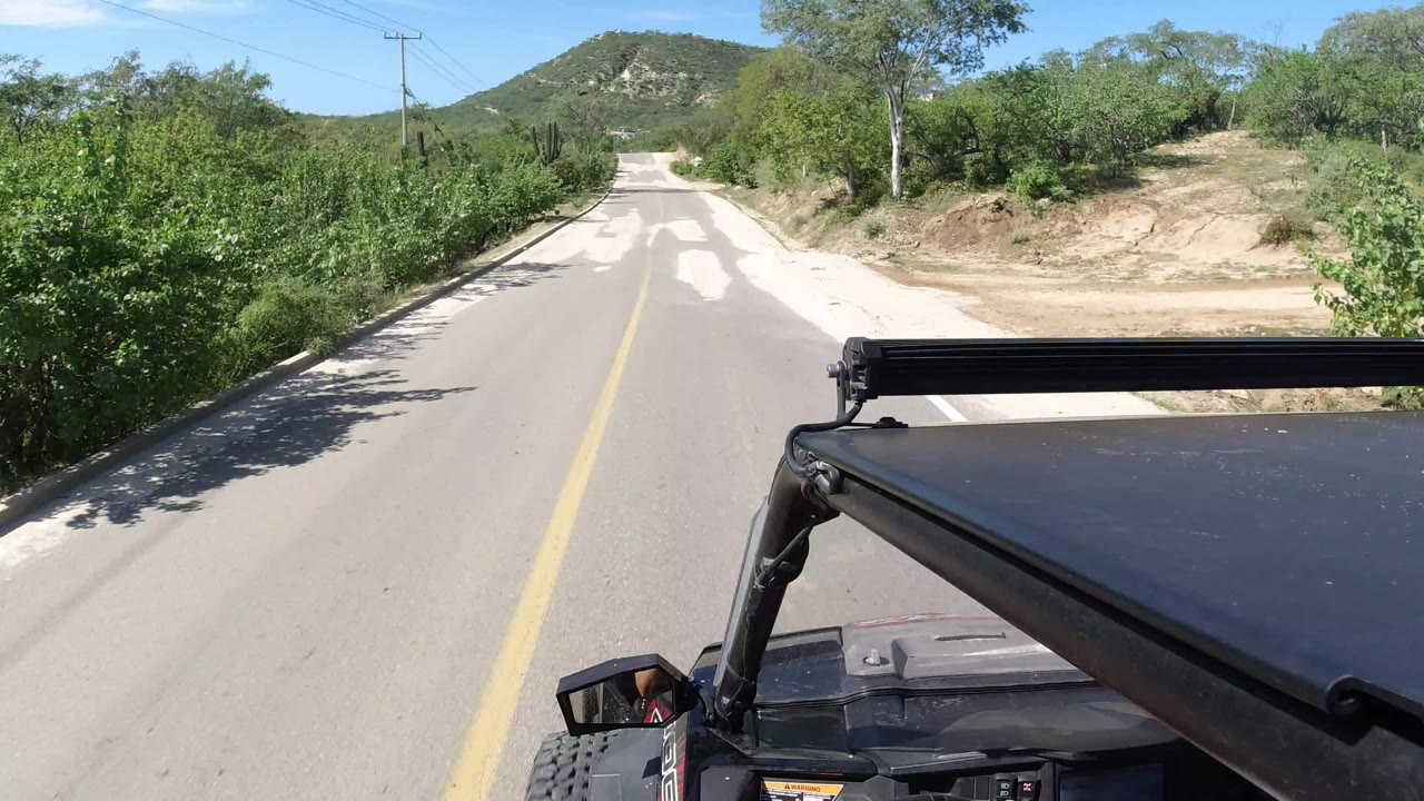 Jeep roof view down a sunlit two-lane road bordered by green brush.
