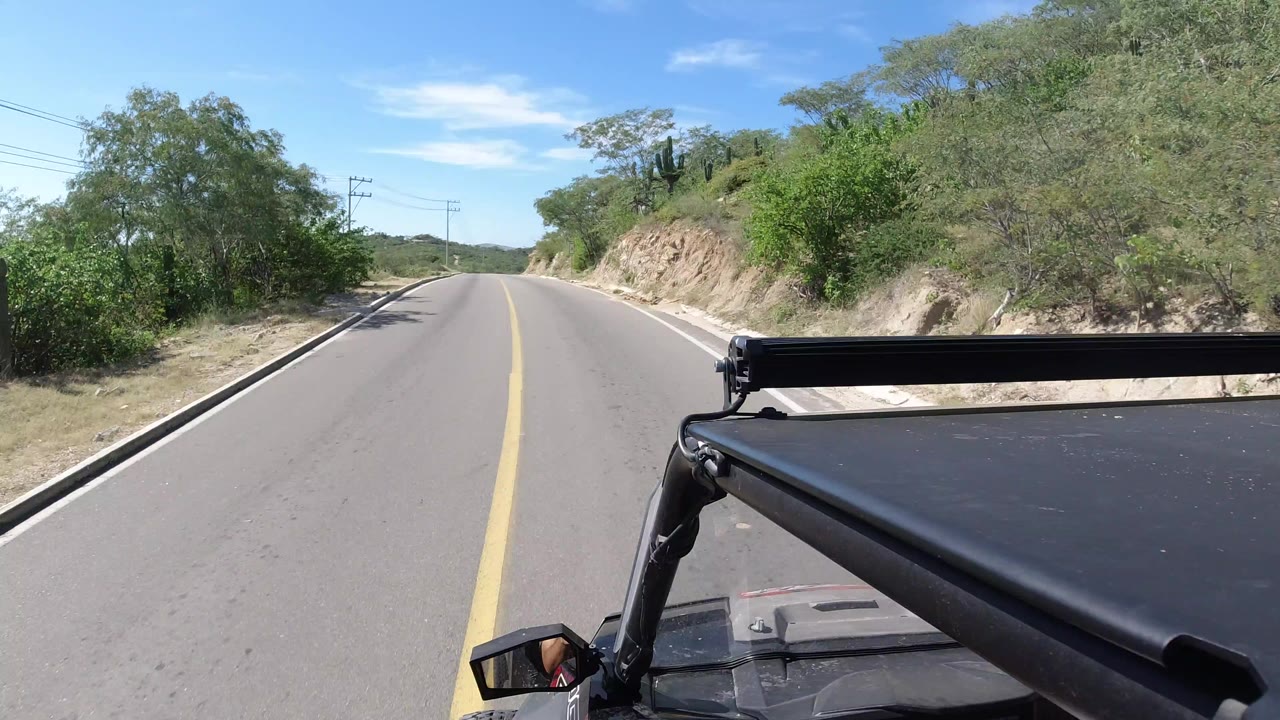 Two-lane road ahead from a black dune buggy with scrub and trees on both sides.