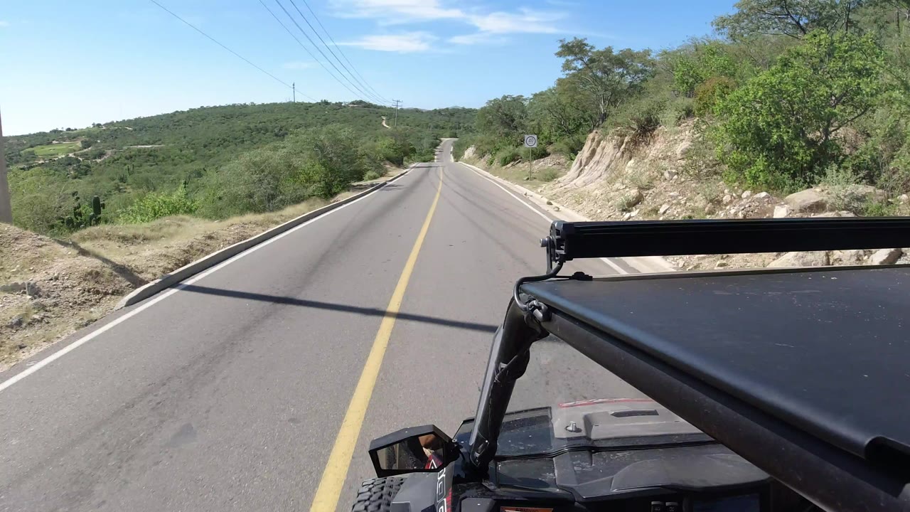 Forward view down a two-lane road with vehicle roof in the foreground