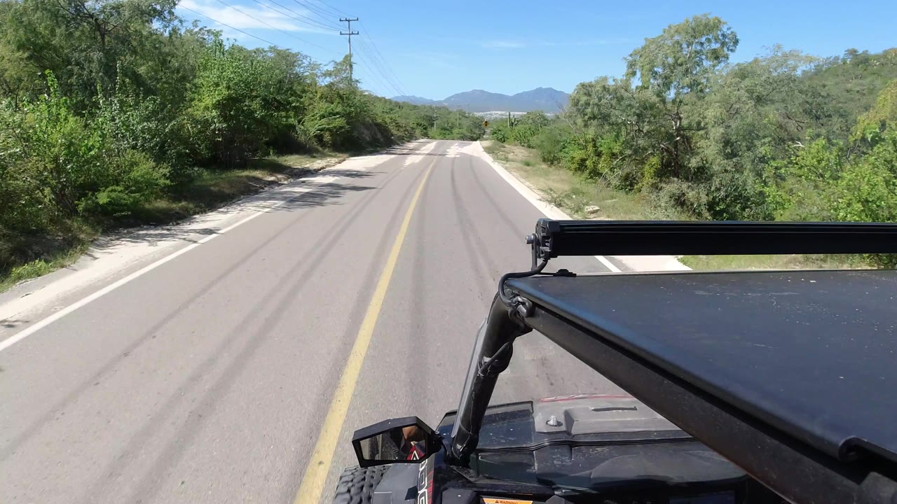 Empty asphalt road curves gently through green desert vegetation and hills.
