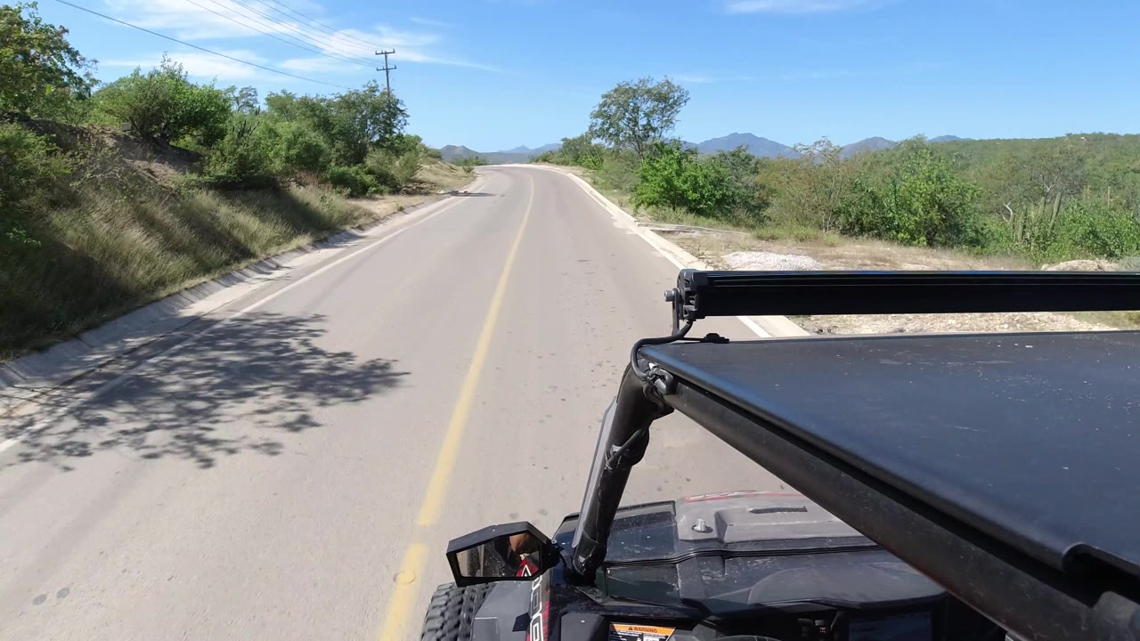Vehicle-mounted road view passing shadowed trees and hillside brush.