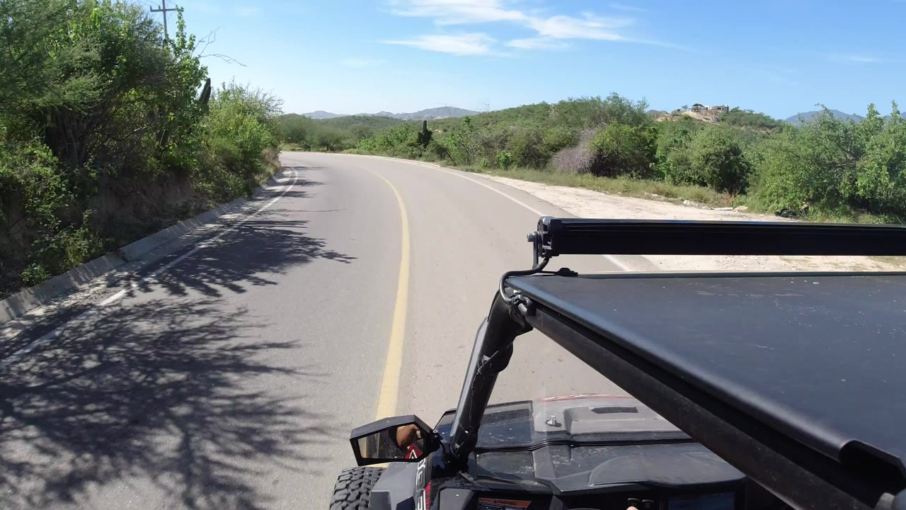 Curving paved road seen from an open vehicle under bright sky.