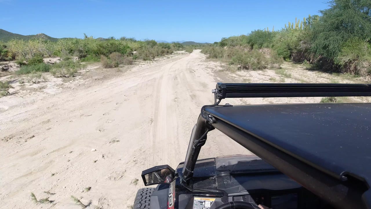 The Los Cabos sandy path continues between low desert bushes, with the black buggy hood and roof support filling the lower right and no visible people.