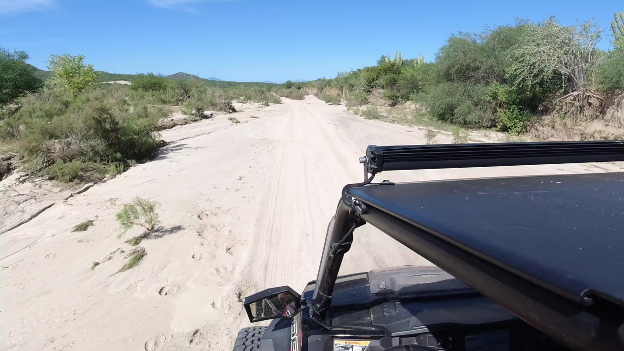 Sandy road seen over the front of a black Wrangler under blue sky.
