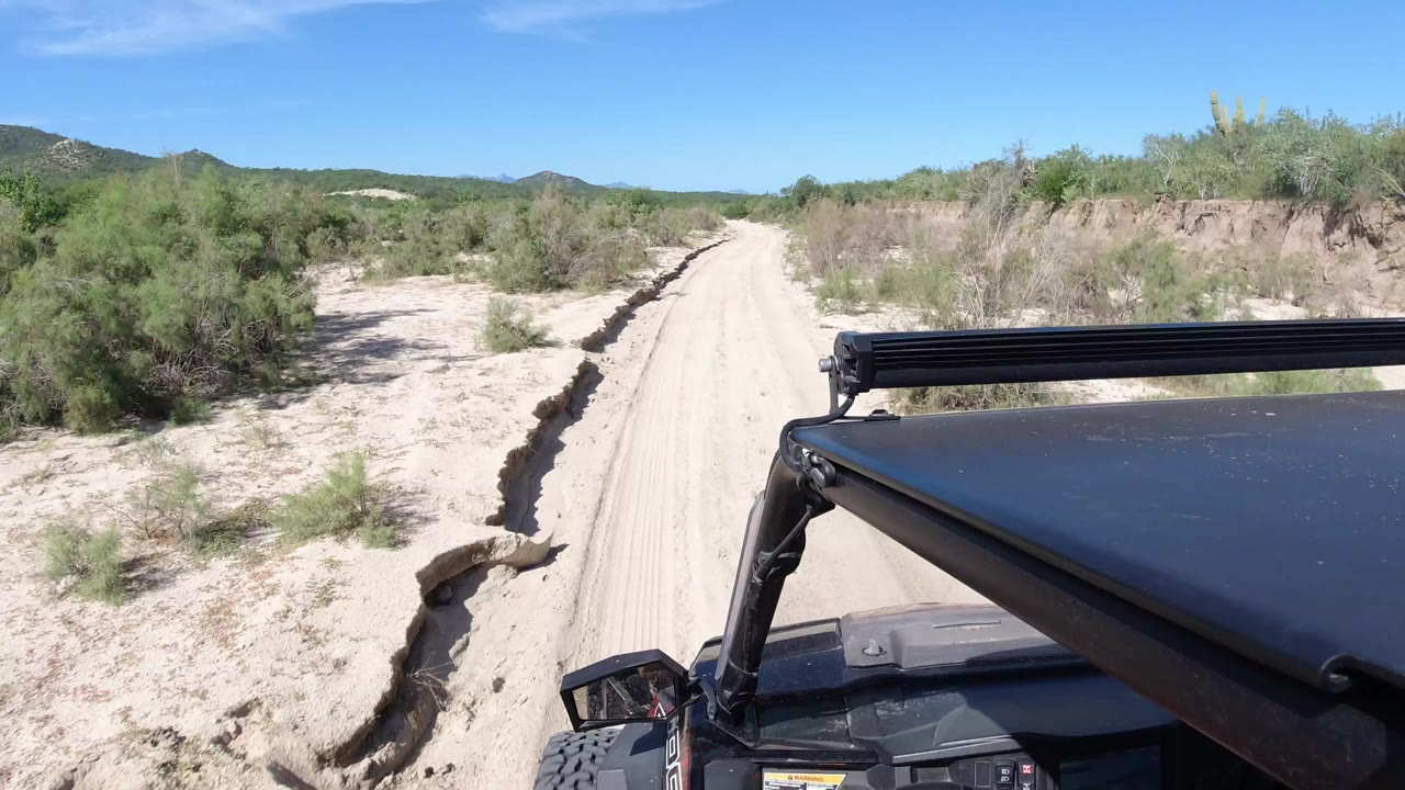 Wrangler roof beside a sandy desert road with green shrubs and low hills.