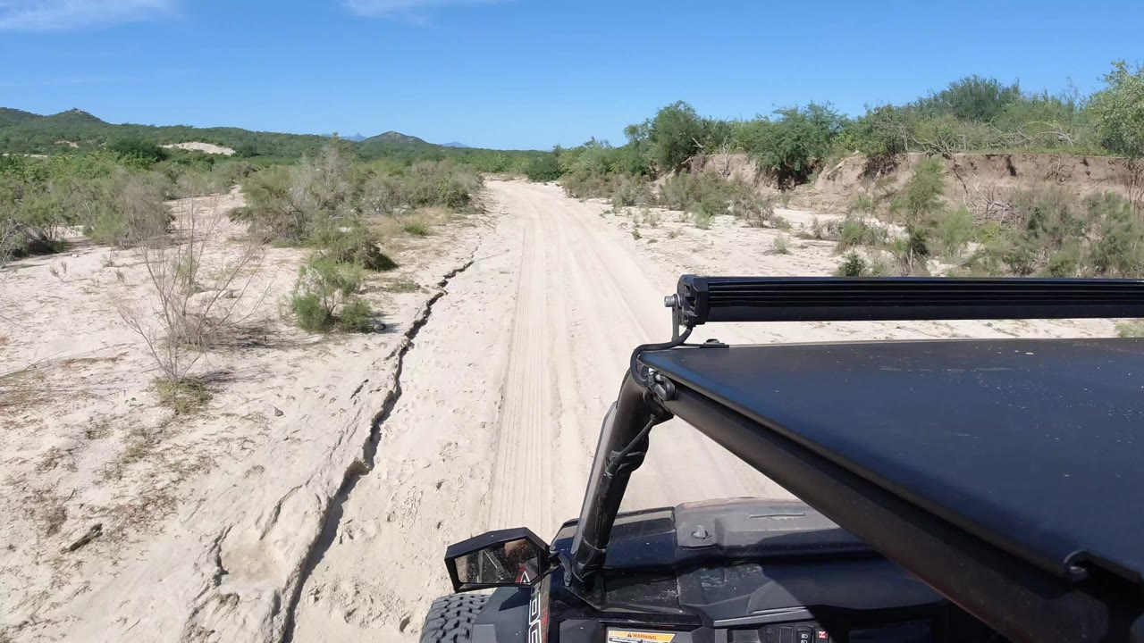 Sandy desert road ahead of an off-road vehicle under blue sky.