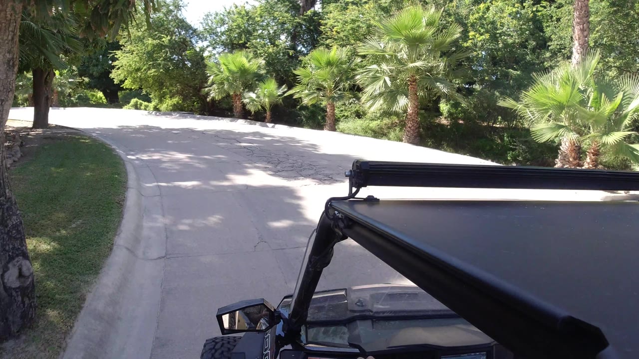 Black Wrangler passing a bright road curve with palms.
