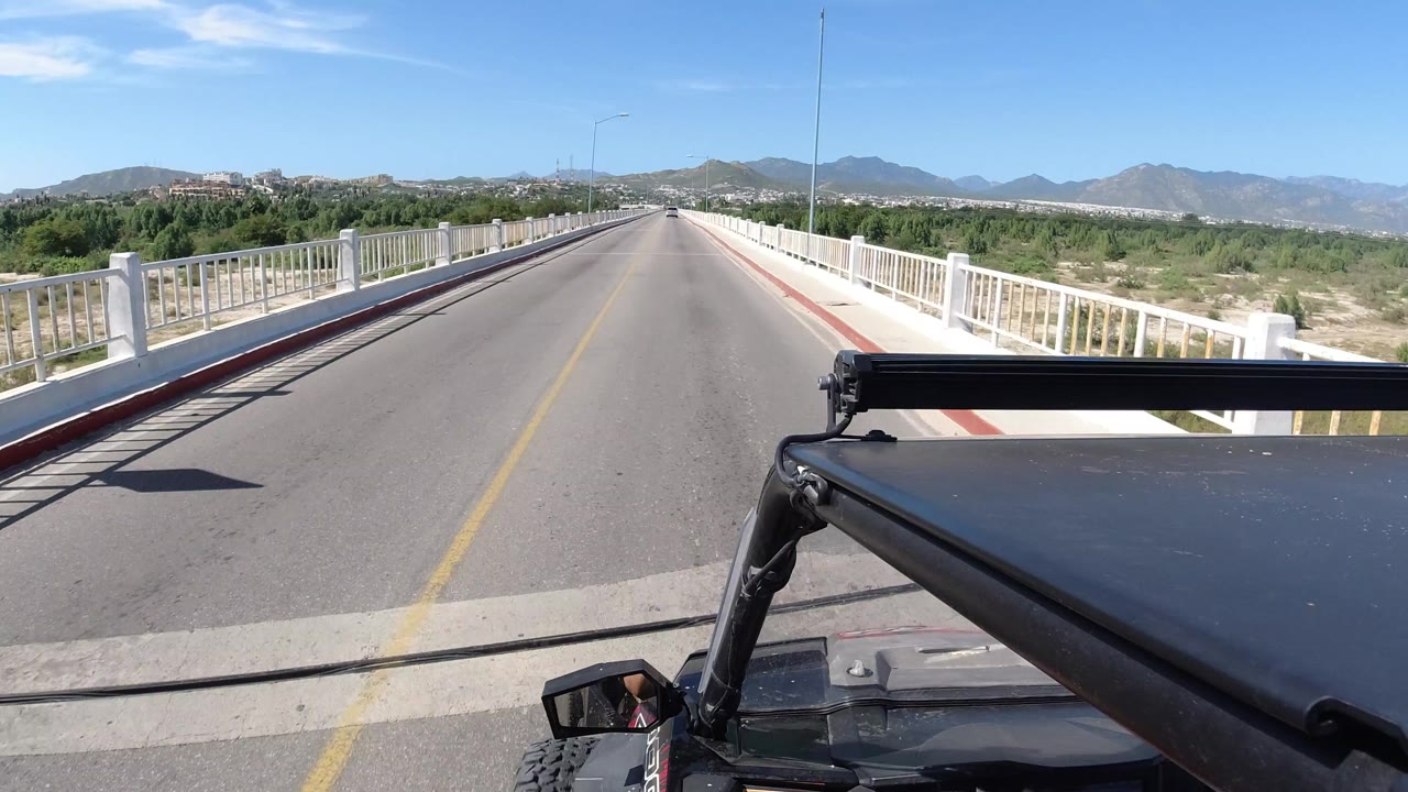 Forward view down a bridge road with white railings and mountains ahead.