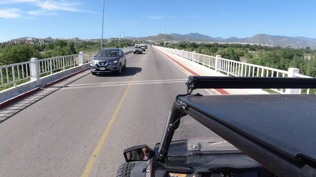 Oncoming car on a bridge with white railings and hills beyond