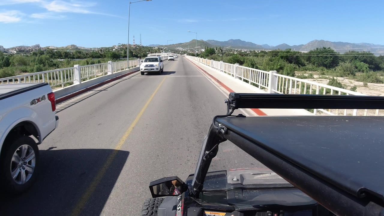 Forward view from a vehicle on a bridge road with a white pickup passing.