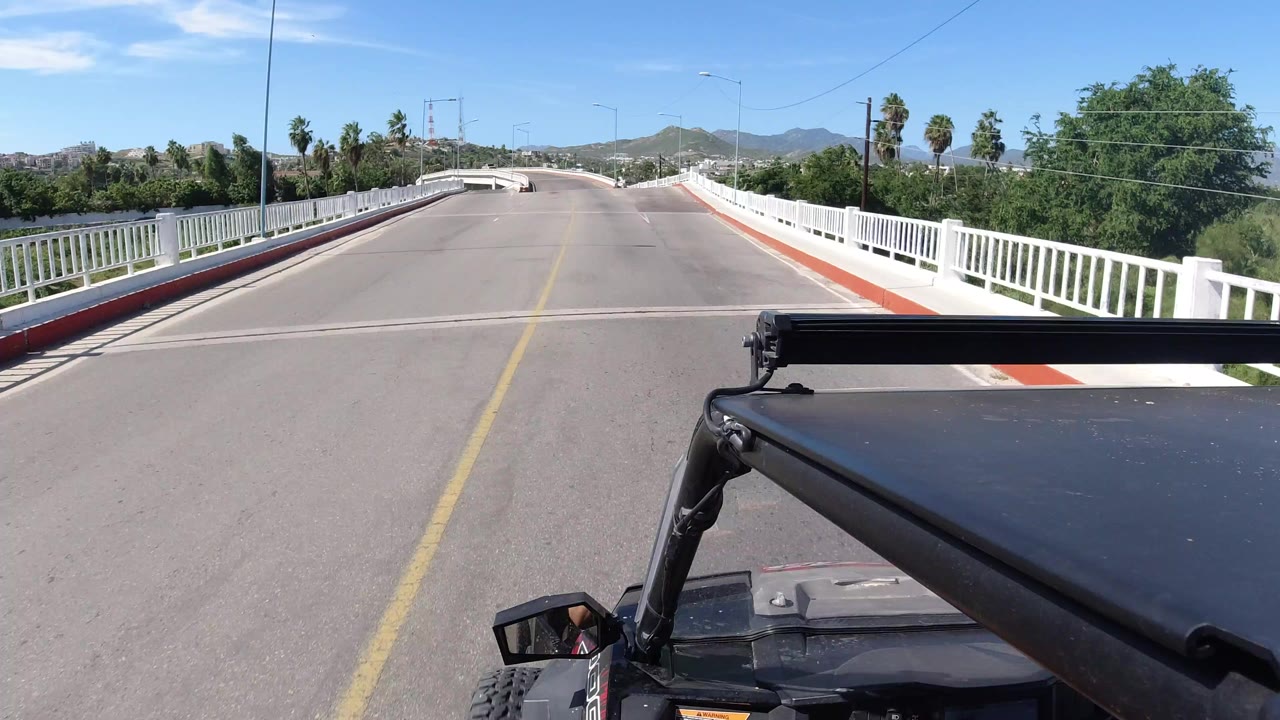 Forward vehicle view on a bridge road with white railings and hills ahead.