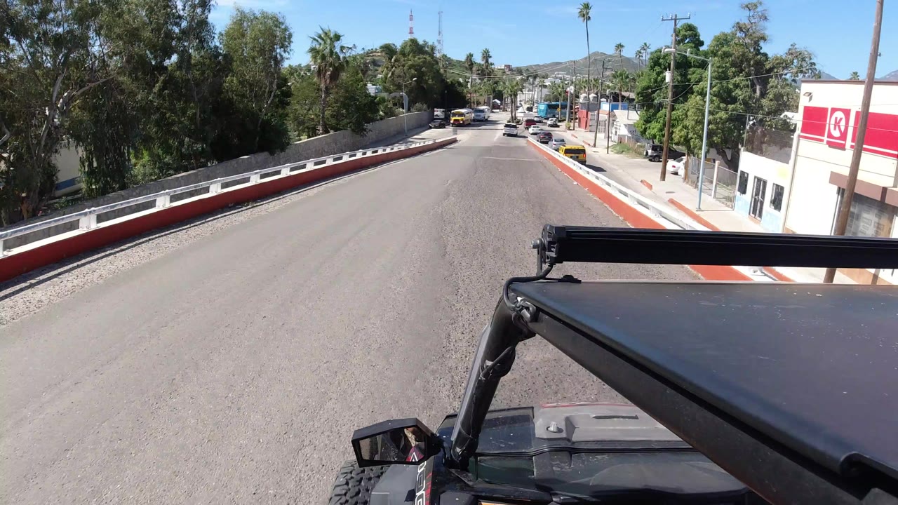 Black Jeep foreground on a sunny paved street with trees and buildings ahead.