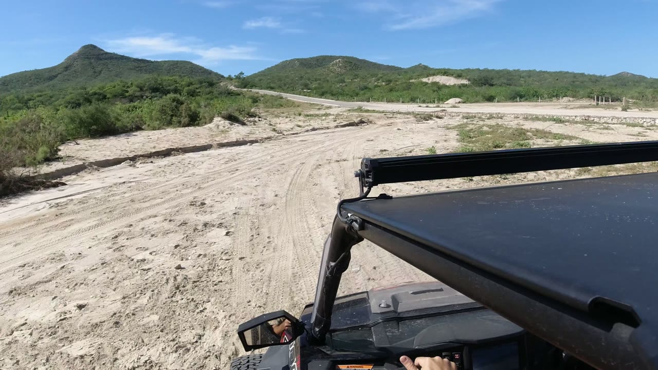 Jeep hood facing a sandy off-road track with green hills ahead.