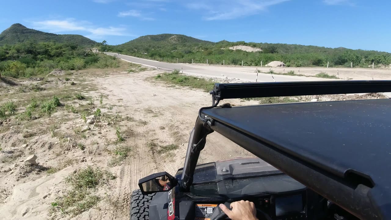 Small black vehicle stopped beside a sandy roadside with hills beyond.