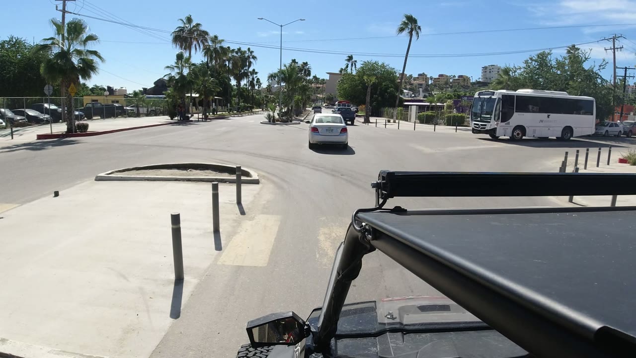 Wrangler foreground at a sunny crossroad with a white bus and white car ahead.