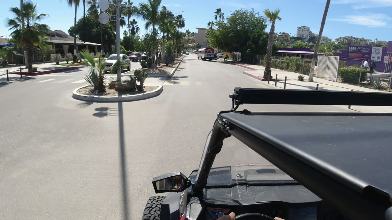 Sunny two-way road seen over a black open vehicle hood.
