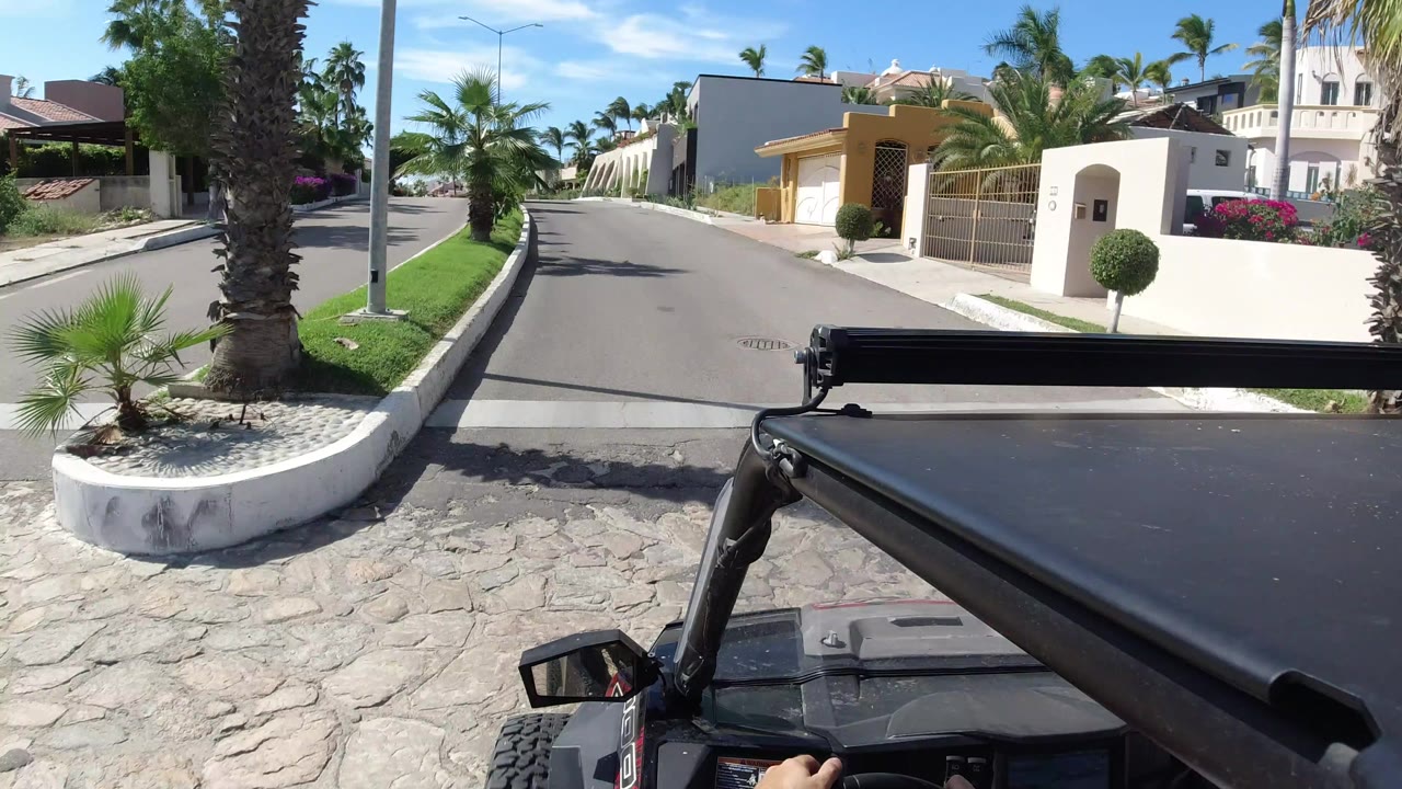 Vehicle foreground on a sunny residential road with palms and gated homes.