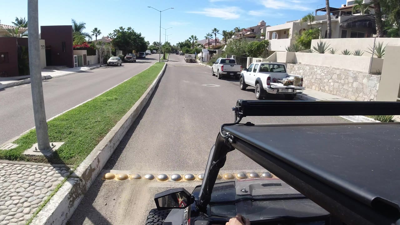 Open vehicle passes directly beside road speed bumps and parked pickup trucks.