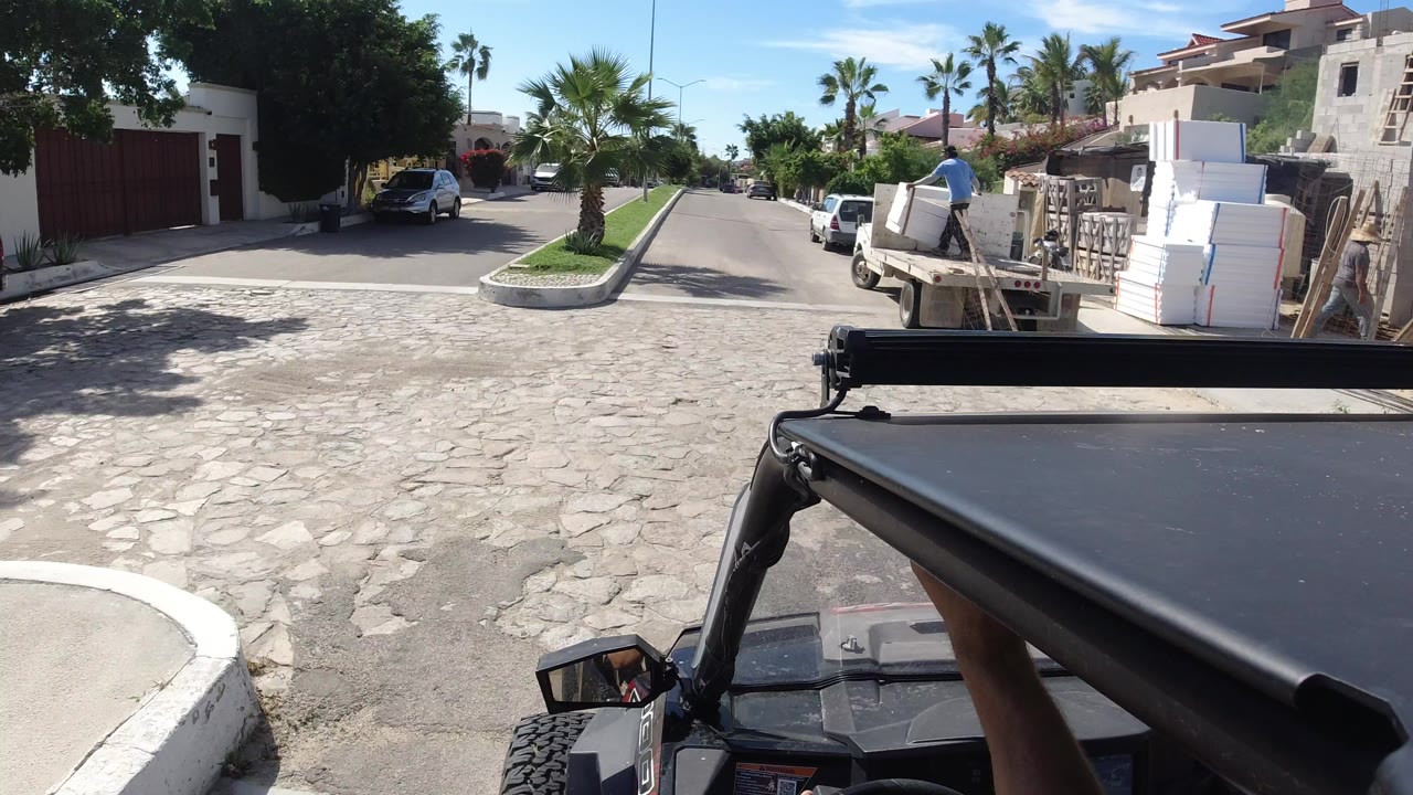 Wrangler foreground on a sunny residential street with a worker near stacked materials.