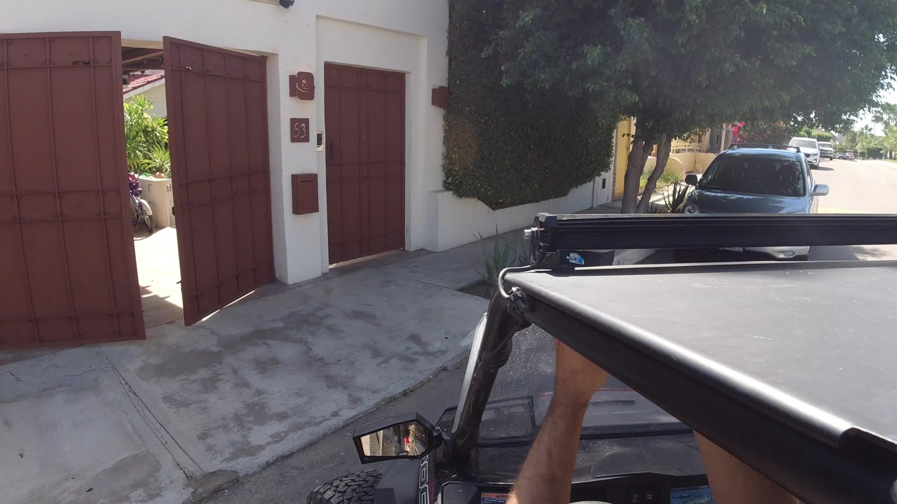 Mounted vehicle view facing red gates and a parked car in bright sun.