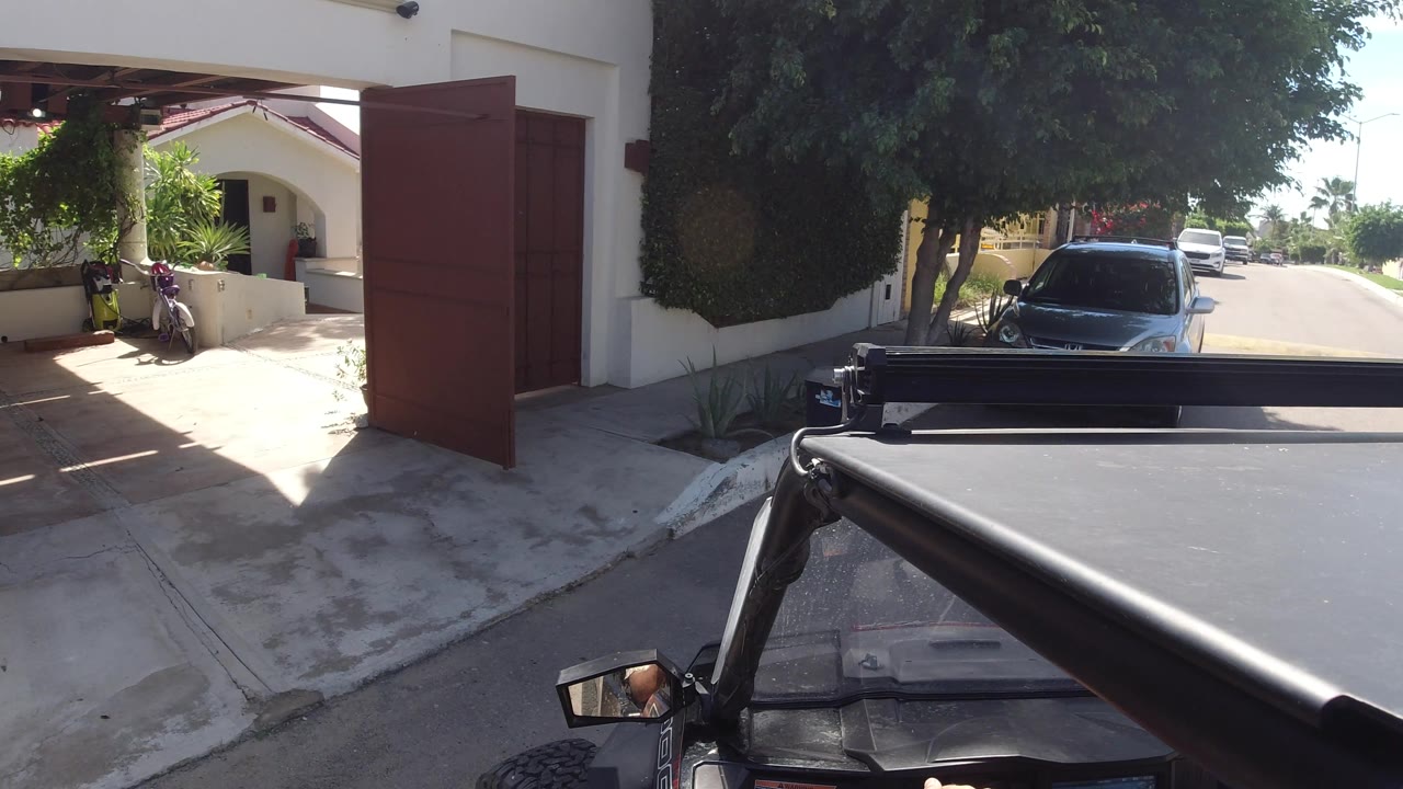 Open gate and driveway with a parked car beside trees.