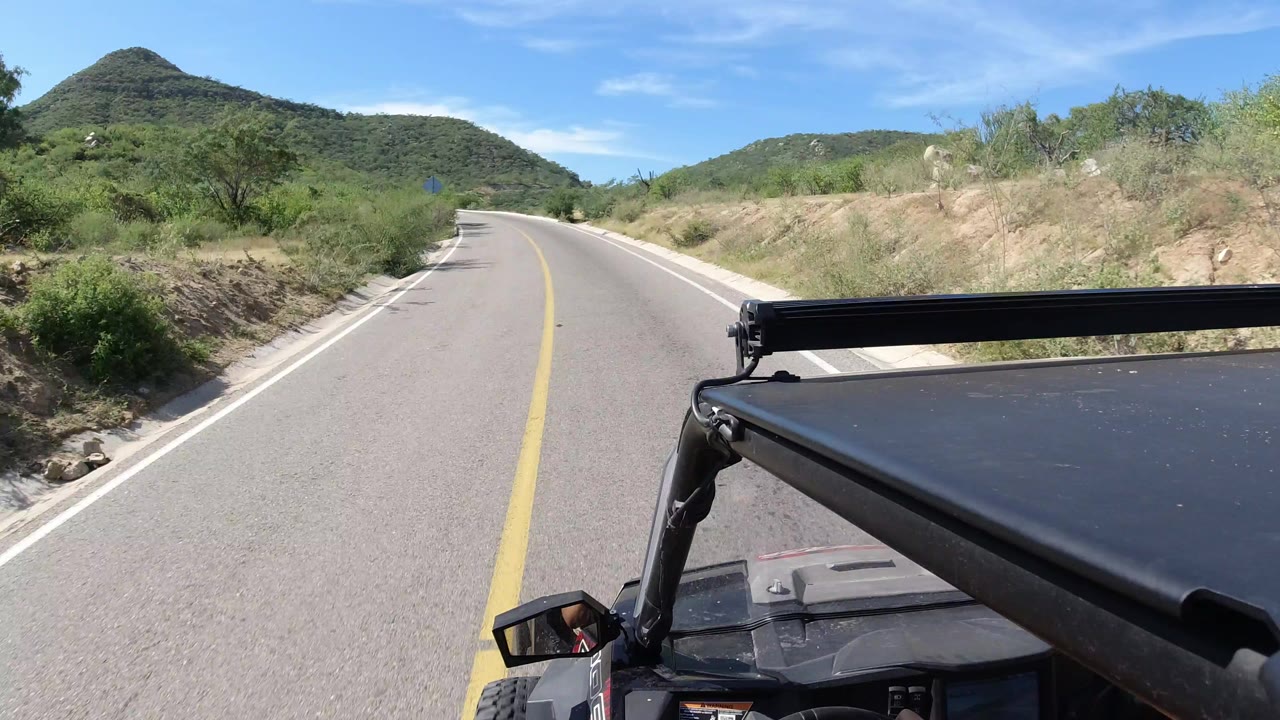 Paved road curving through green hills with Wrangler roof in foreground