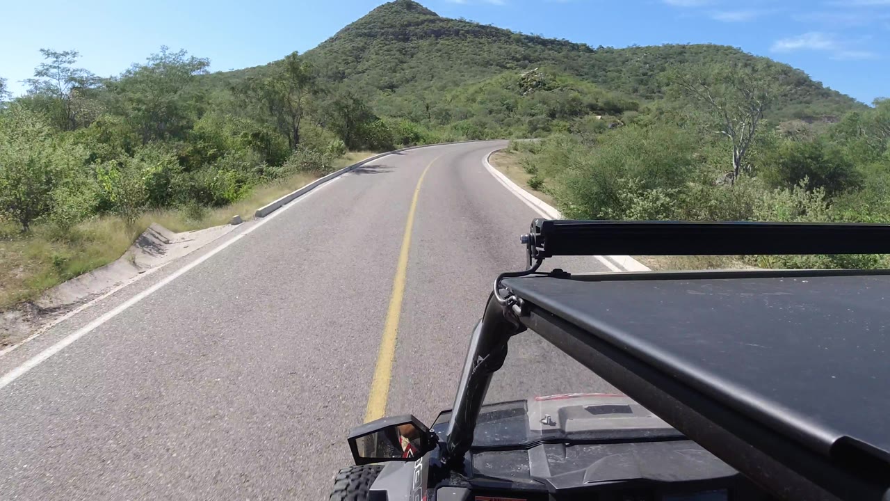 Curving road with hillside vegetation and a Wrangler frame in the foreground.