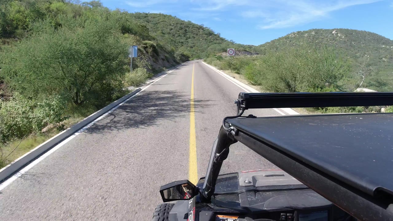 Mountain road passing roadside signs and brush.