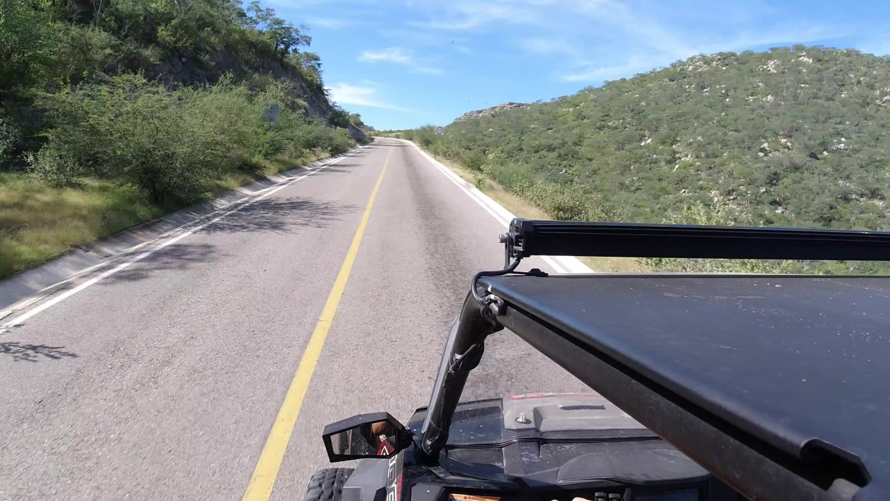 Forward view from a vehicle on a narrow road between green hills.