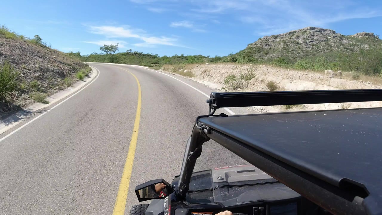 Curving paved road seen from an open vehicle with rocky hillside ahead.