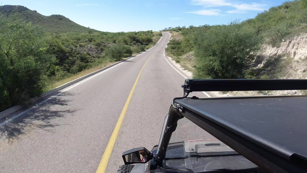 Two-lane road through green scrub with vehicle roof in foreground.