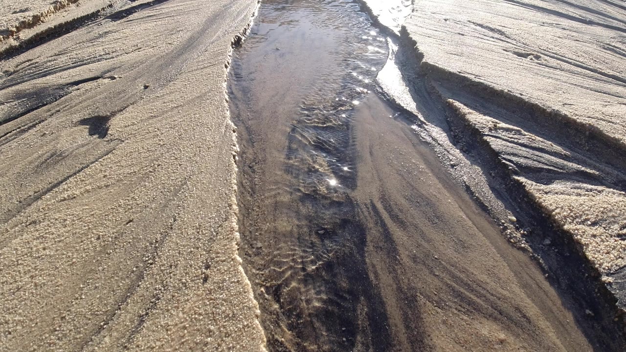 Shallow water channel cutting through tan sand.