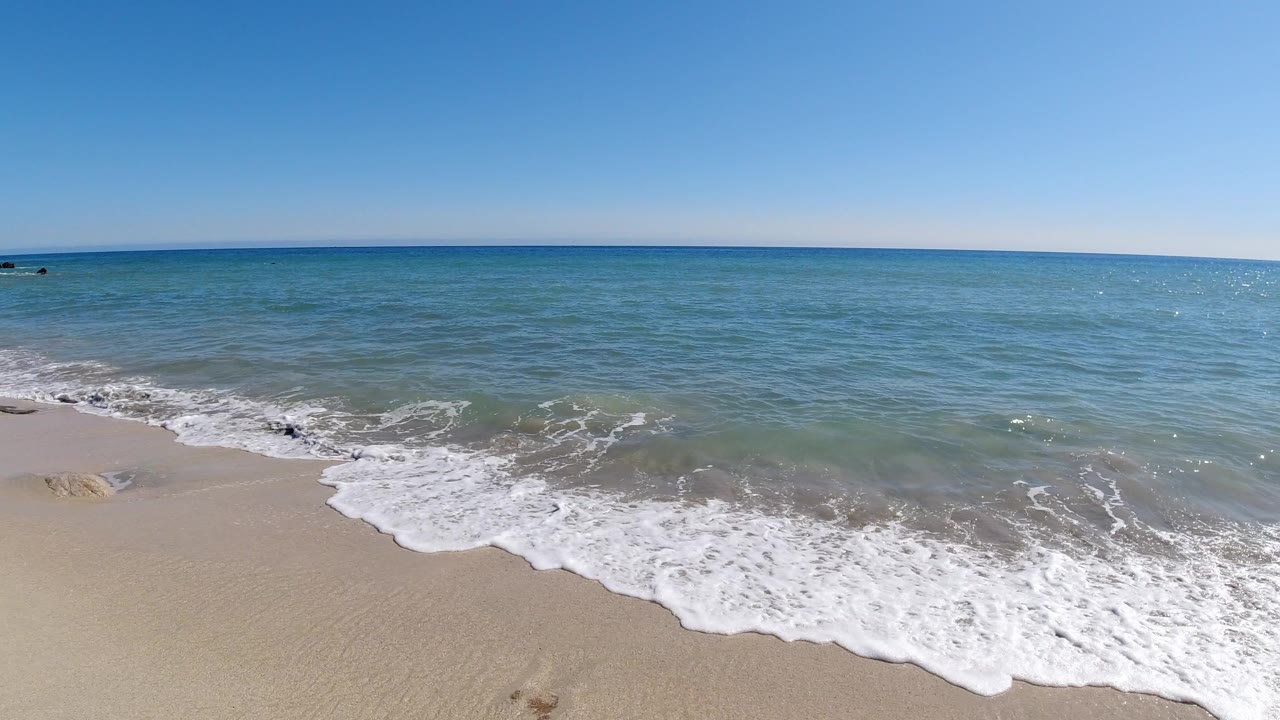 Small wave washing onto pale sand under a blue sky.