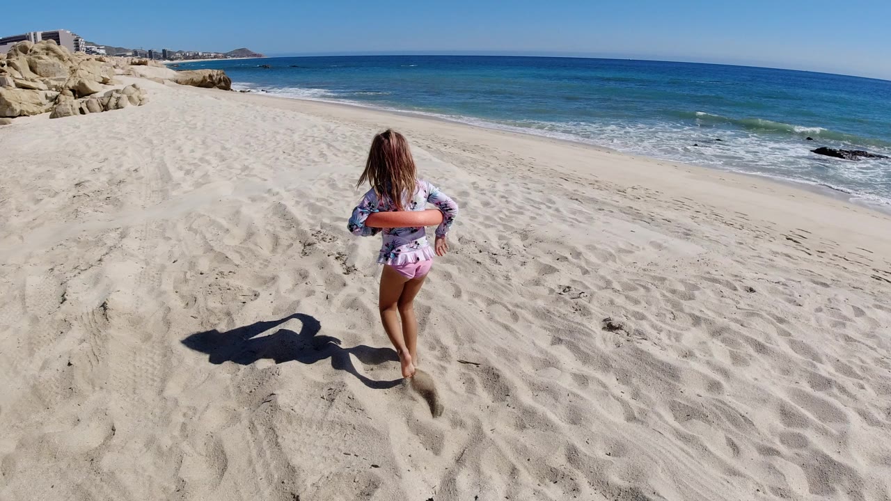 Young girl running away from camera on a sandy beach beside the ocean.