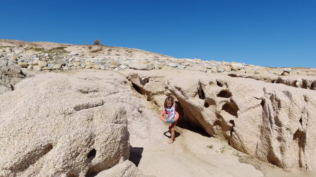 Young girl standing between pale rocks on a sandy beach.