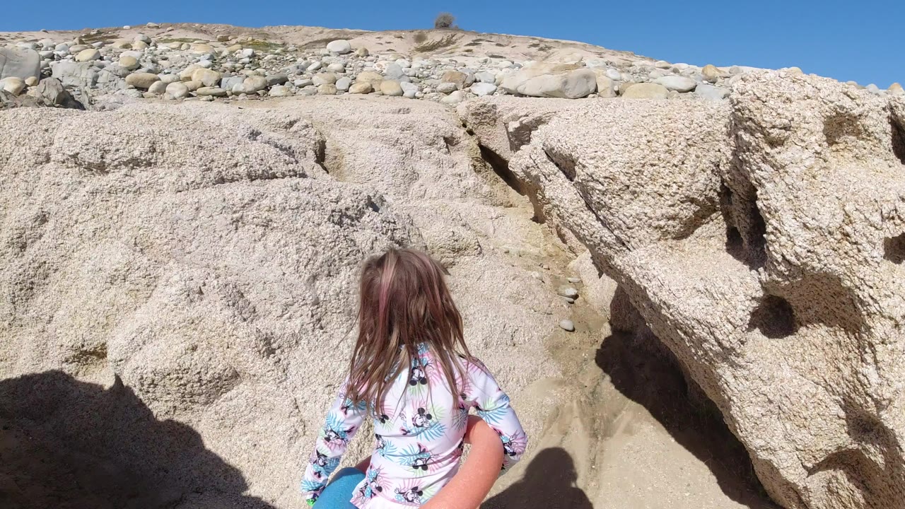 Young girl facing pale rocky terrain under blue sky.