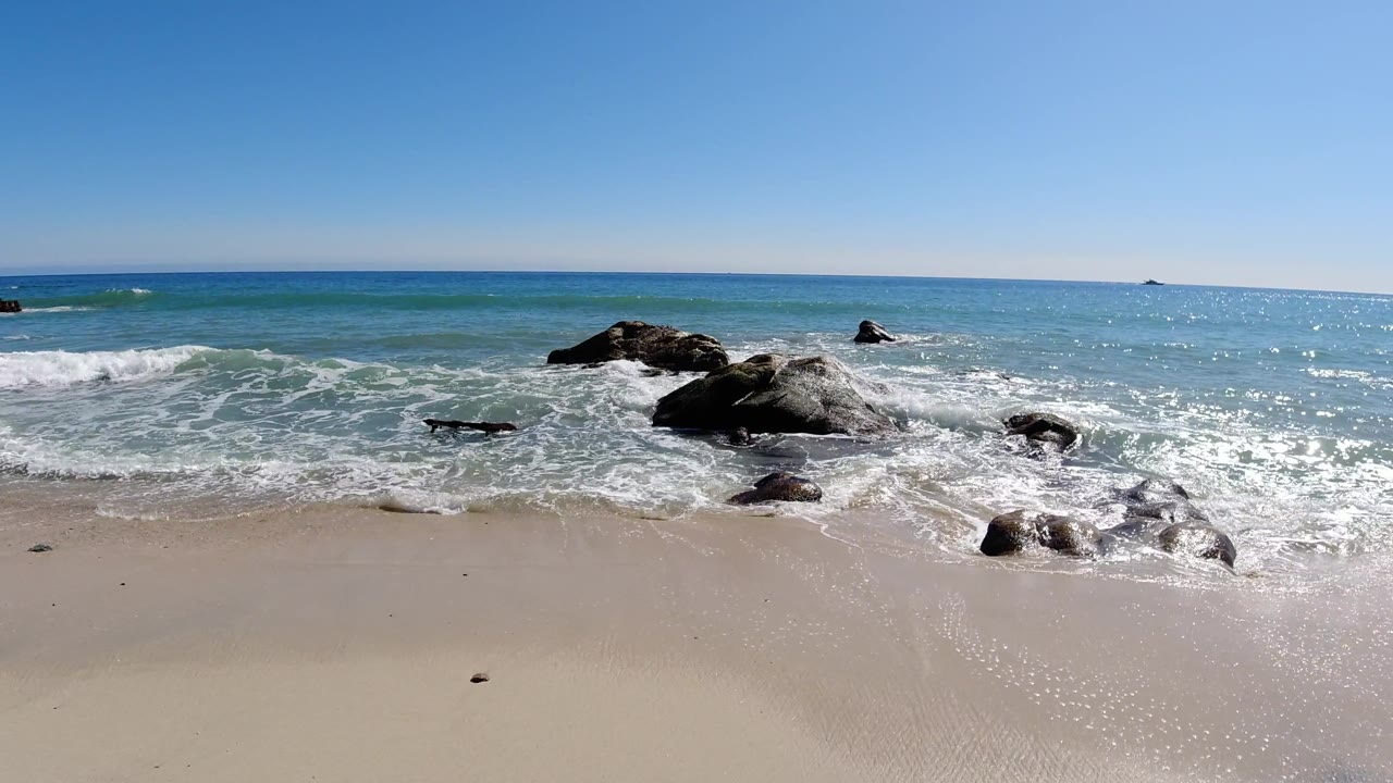 Foamy surf spreading across sand beside shoreline rocks.