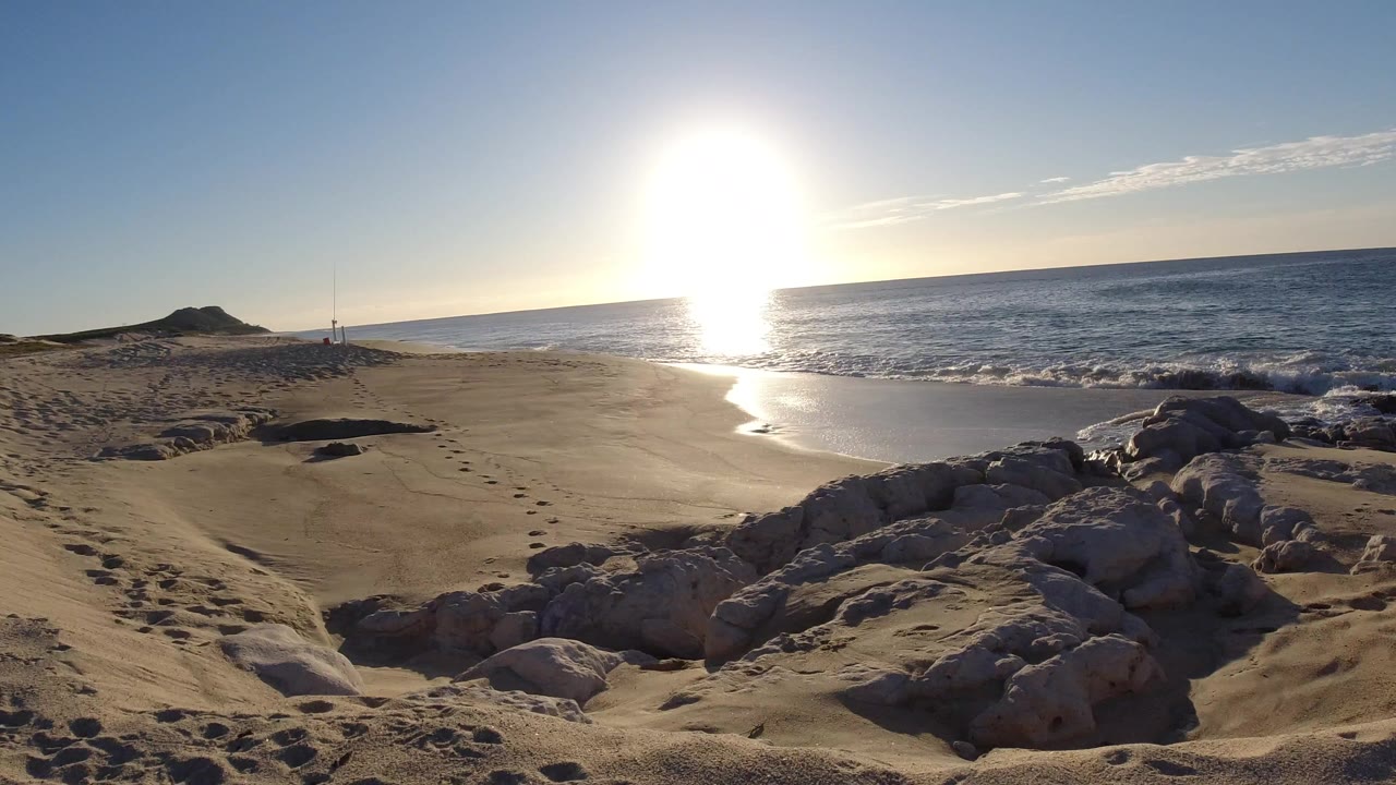 Sunlit beach with rocks, footprints, and waves