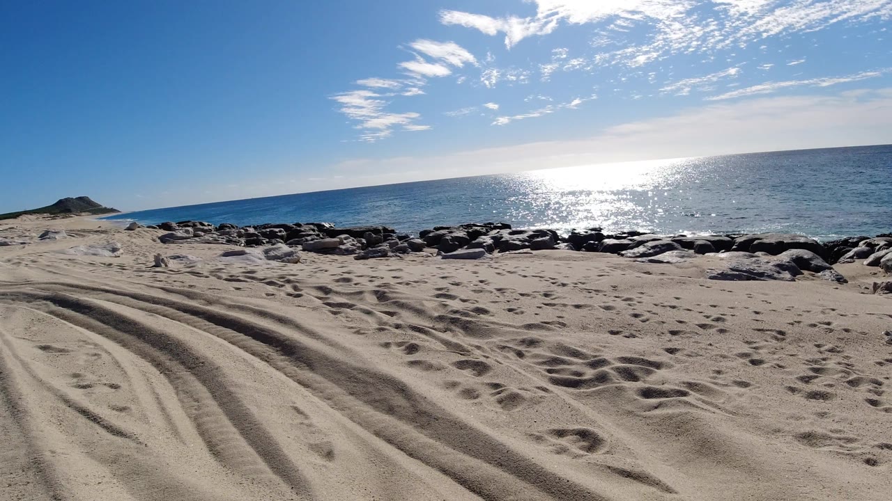 Empty sandy beach with rocks and ocean under a bright sky.
