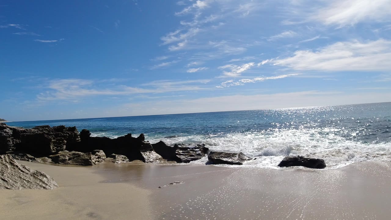 Rocky beach with waves under a bright blue sky.