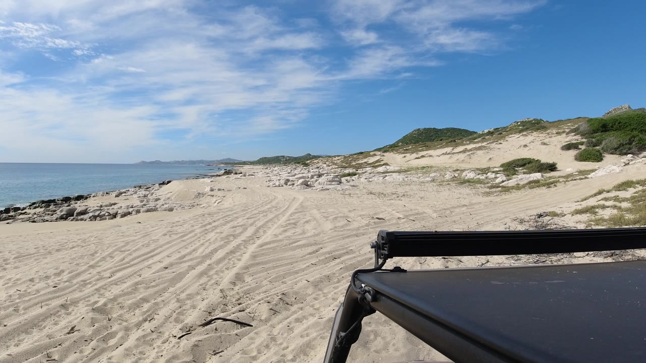 Wide beach and ocean view with dunes and a dark structure at the lower right.