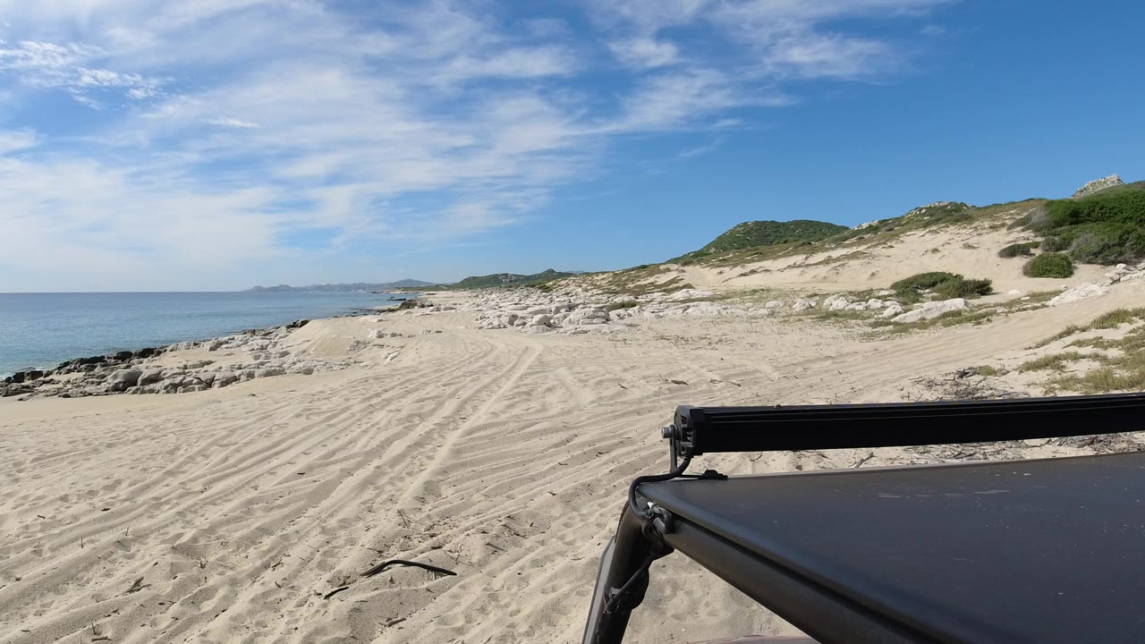 White sand beach with ocean, dunes, and black vehicle roof in foreground.