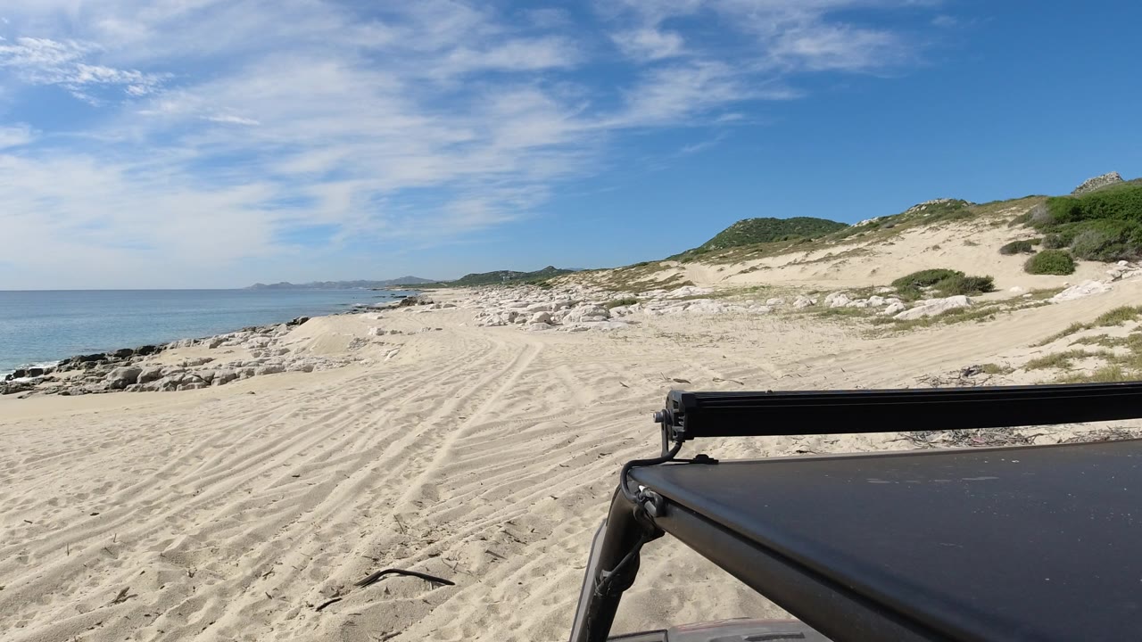 Jeep-mounted beach view with ocean, rocks, sand, and dunes.