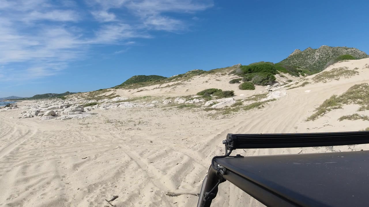 Jeep roof and light bar beside sandy dunes under blue sky.