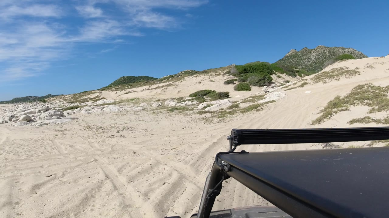 Jeep foreground facing sandy tracks and dunes under blue sky.