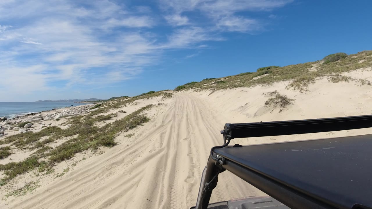 Rutted sand path climbs between dunes under a blue sky.