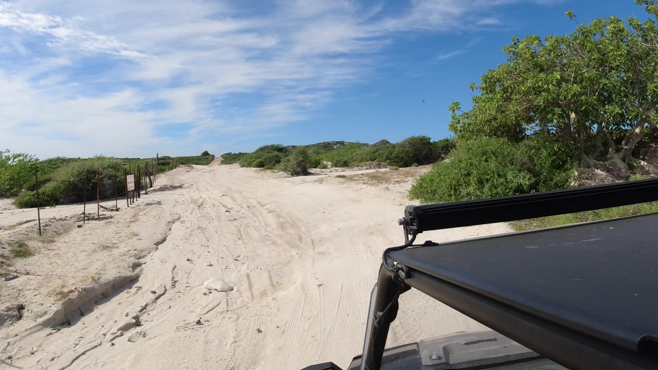 Wide sandy track with scrub vegetation and vehicle roof corner